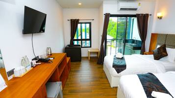 Habitación de hotel con escritorio de madera, televisor de pantalla plana, cama con ropa blanca y balcón con vistas a zonas verdes.