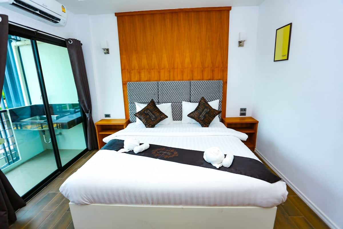 A hotel room with a large bed, a wooden headboard, and a sliding glass door to a balcony.