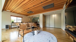 Een moderne woonkamer met een houten plafond, een rond vloerkleed en een eethoek met rieten stoelen.