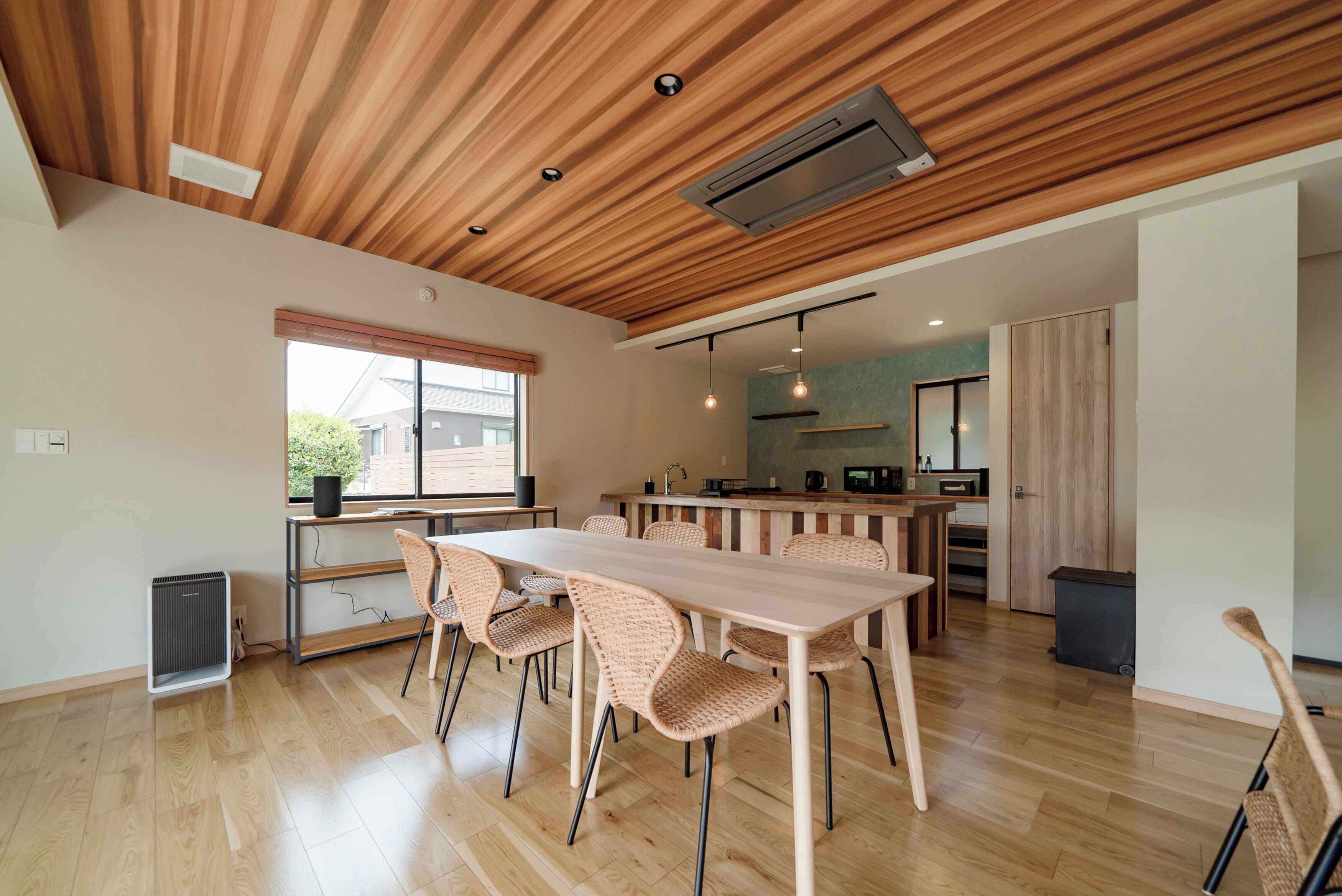Una cocina moderna con techo de madera, un comedor con sillas de mimbre y vista al exterior.