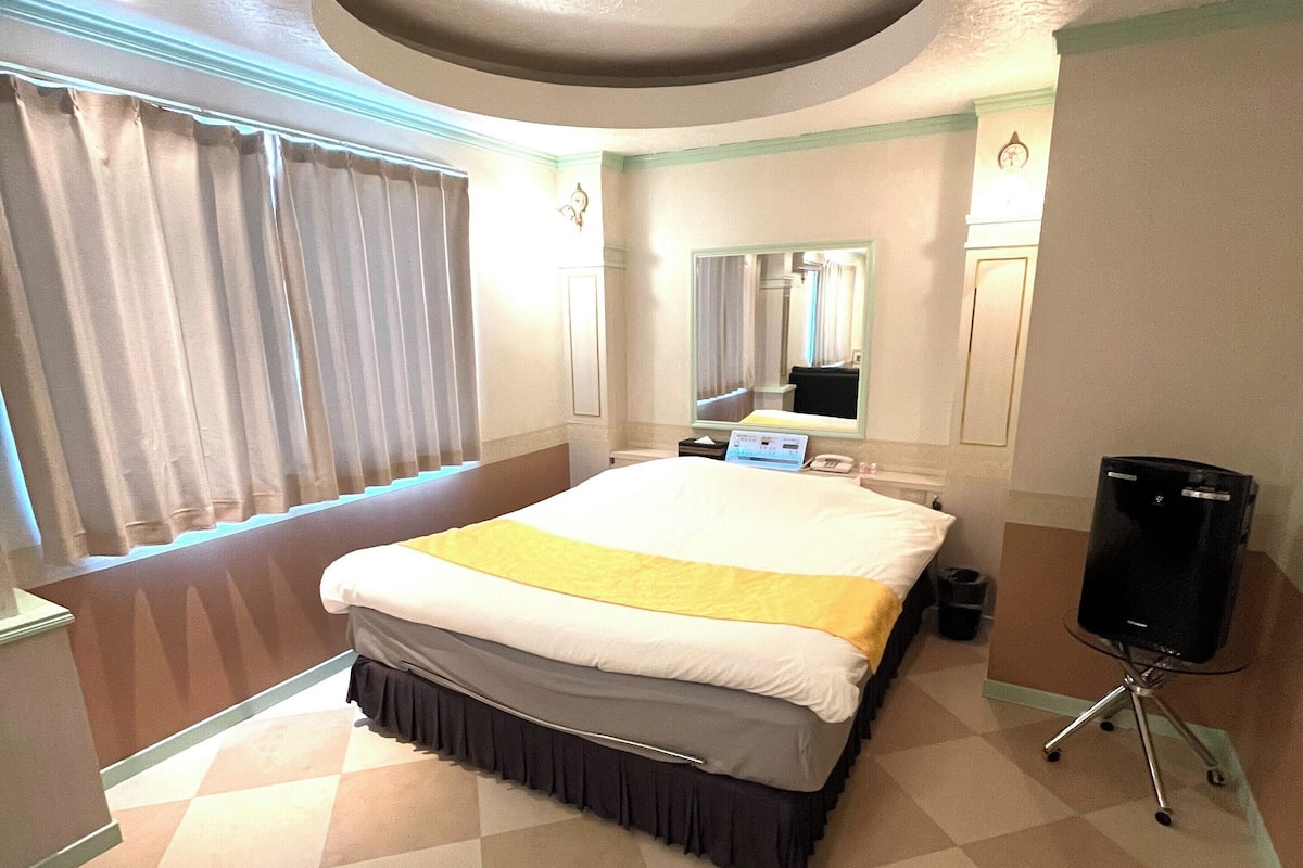 A hotel room with a large bed, a bedside table, a mirror, a clock, and a television on a stand.