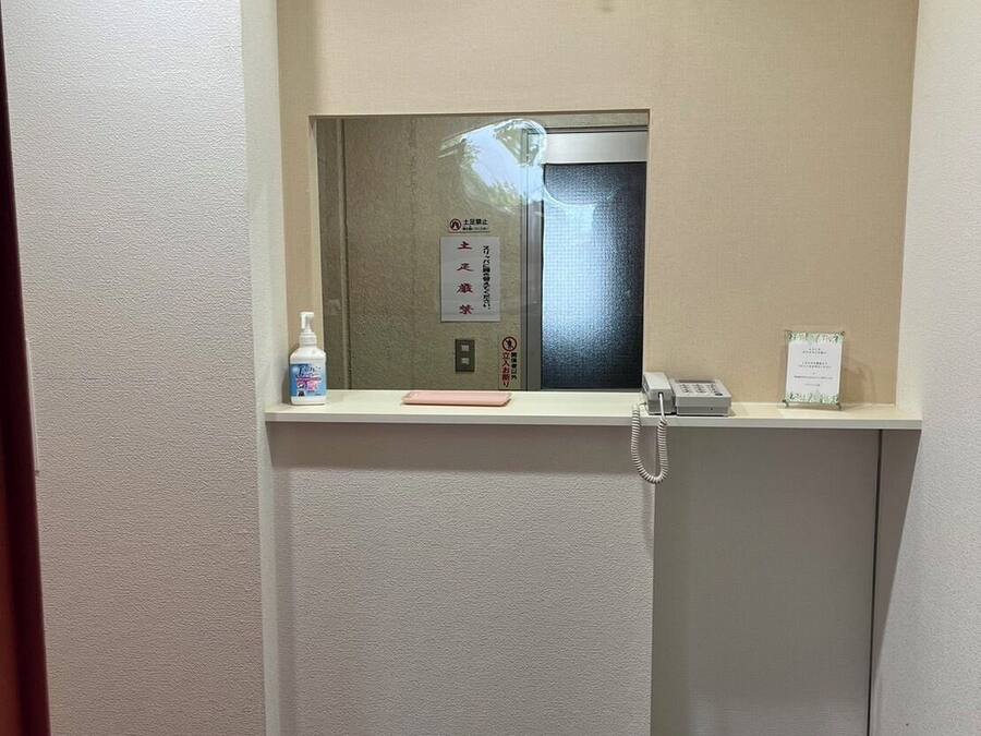 Pequeño espacio de ascensor cerrado, con un teléfono, una caja de pañuelos y un dispensador de desinfectante.