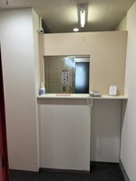 Pequeño espacio de ascensor cerrado, con un teléfono, una caja de pañuelos y un dispensador de desinfectante.