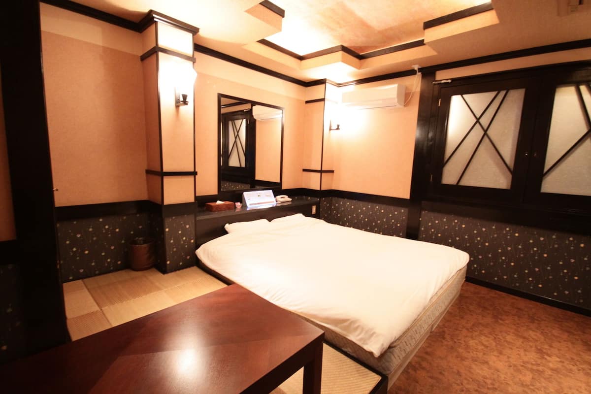 A hotel room with a bed, a bedside table, a mirror, and a window with a decorative screen.