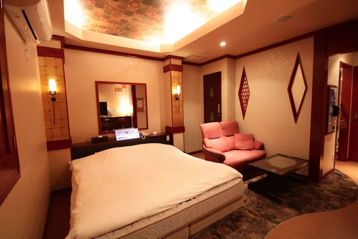 A hotel room with a bed, a desk with a laptop, a chair, and a small table.