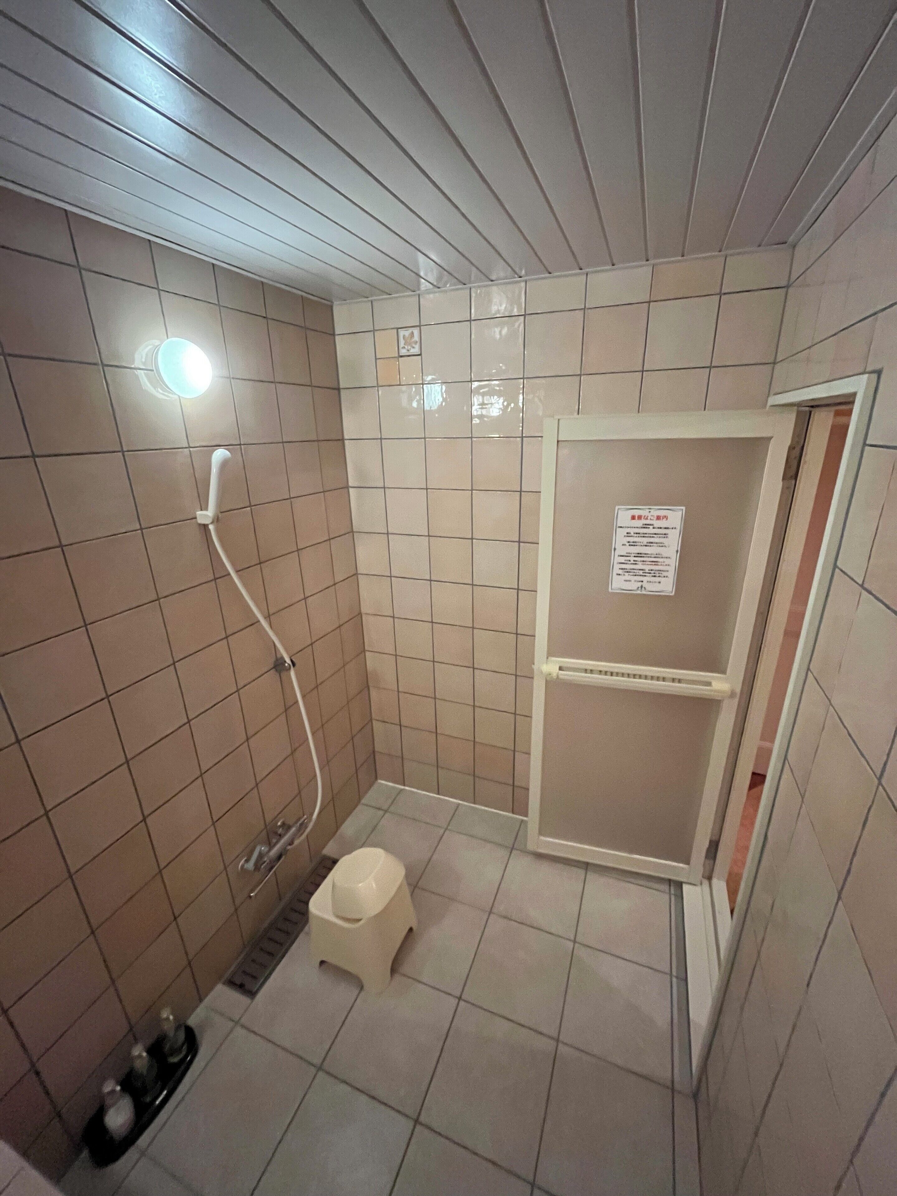 A small, tiled bathroom with a shower, toilet, and a shelf unit.