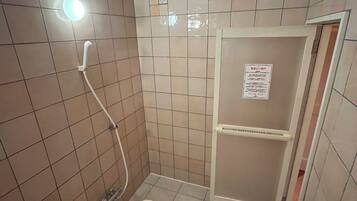 A small, tiled bathroom with a shower, toilet, and a shelf unit.