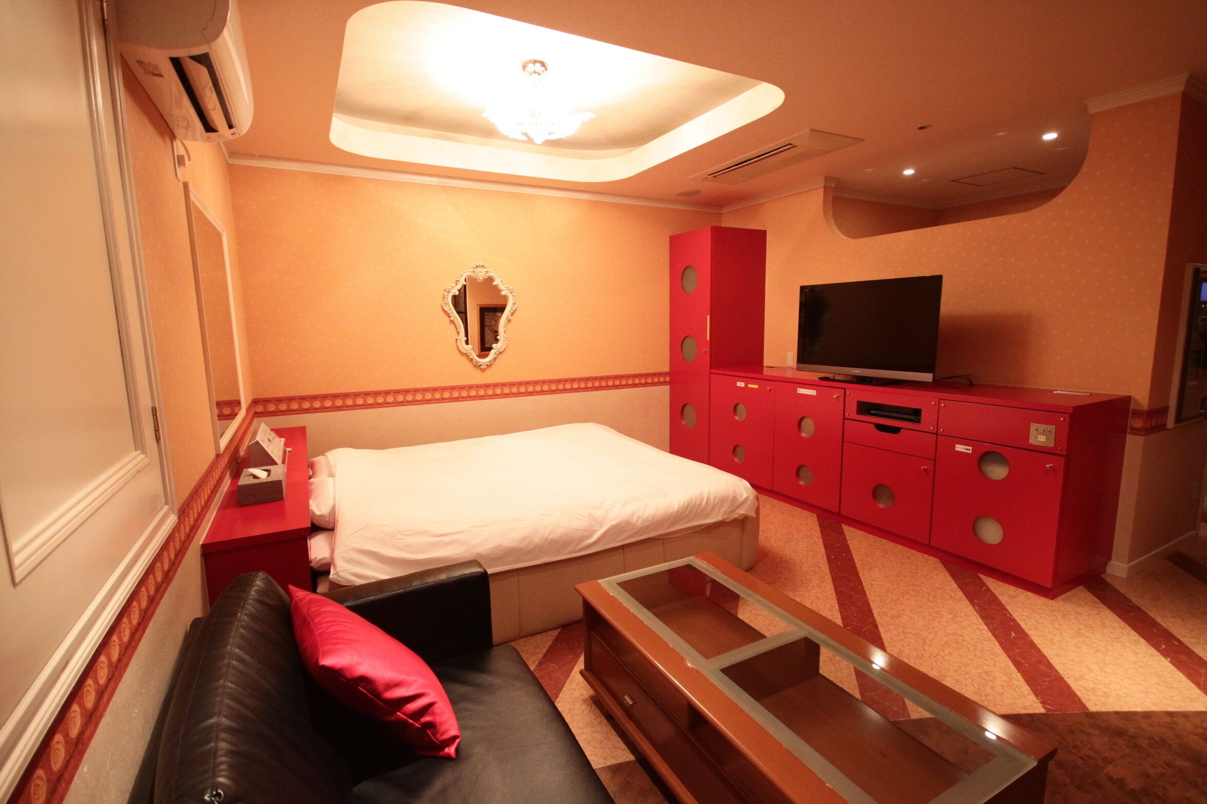 A hotel room with a bed, a red dresser, a television, and a small table.