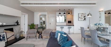 A modern living room with a grey sofa, a dining area with grey chairs, and a kitchen in the background.
