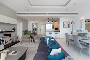 Een moderne woonkamer met een grijze bank, een eethoek met grijze stoelen en een keuken op de achtergrond.