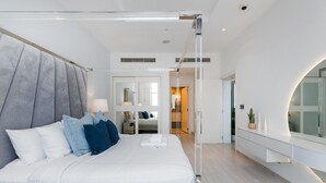 A modern bedroom with a large bed, a bedside table with a lamp, a mirror, and a view of the hallway.