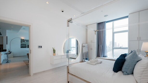 Une chambre moderne dotée d’un grand lit, d’un dressing, d’une salle de bain et offrant une vue sur la ville.