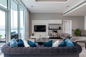 Een moderne woonkamer met een groot raam, een flatscreen televisie en een bank met blauwe en witte kussens.