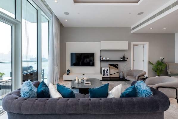A modern living room with a large window, a flat-screen TV, and a sofa with blue and white cushions.