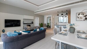 A modern living room with a grey sofa, a flat-screen TV, and a dining area with a white table and chairs.