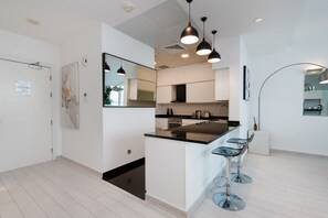 A modern kitchen with a central island, bar stools, pendant lighting, and a large mirror.
