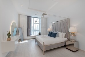 A modern bedroom with a four-poster bed, a bedside table with a lamp, a large mirror, and a potted plant.