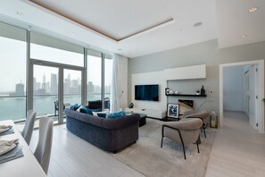 Een moderne woonkamer met een groot raam met uitzicht op een stadsgezicht, een grijze bank, een eethoek en een flatscreen televisie aan de muur.