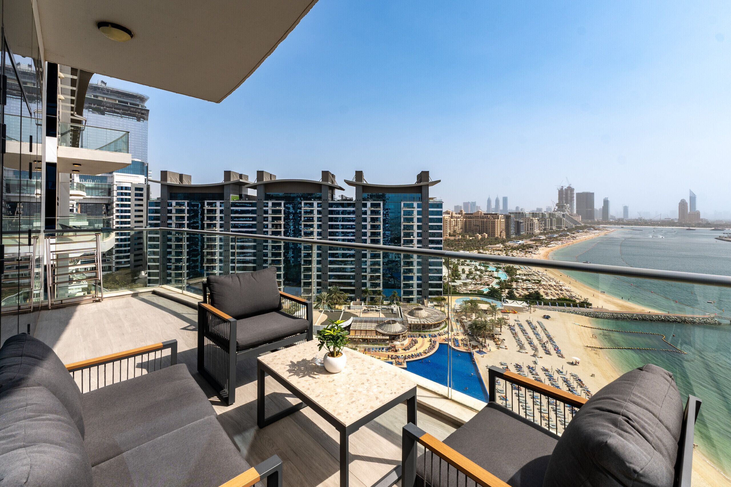 Ein Balkon mit Blick auf Strand und Stadtlandschaft, ausgestattet mit einer Couch, Stühlen und einem Tisch.