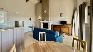 Een ruime woonkamer met een houten eettafel, een blauwe bank en een keuken met een koelkast en een spoelbak.