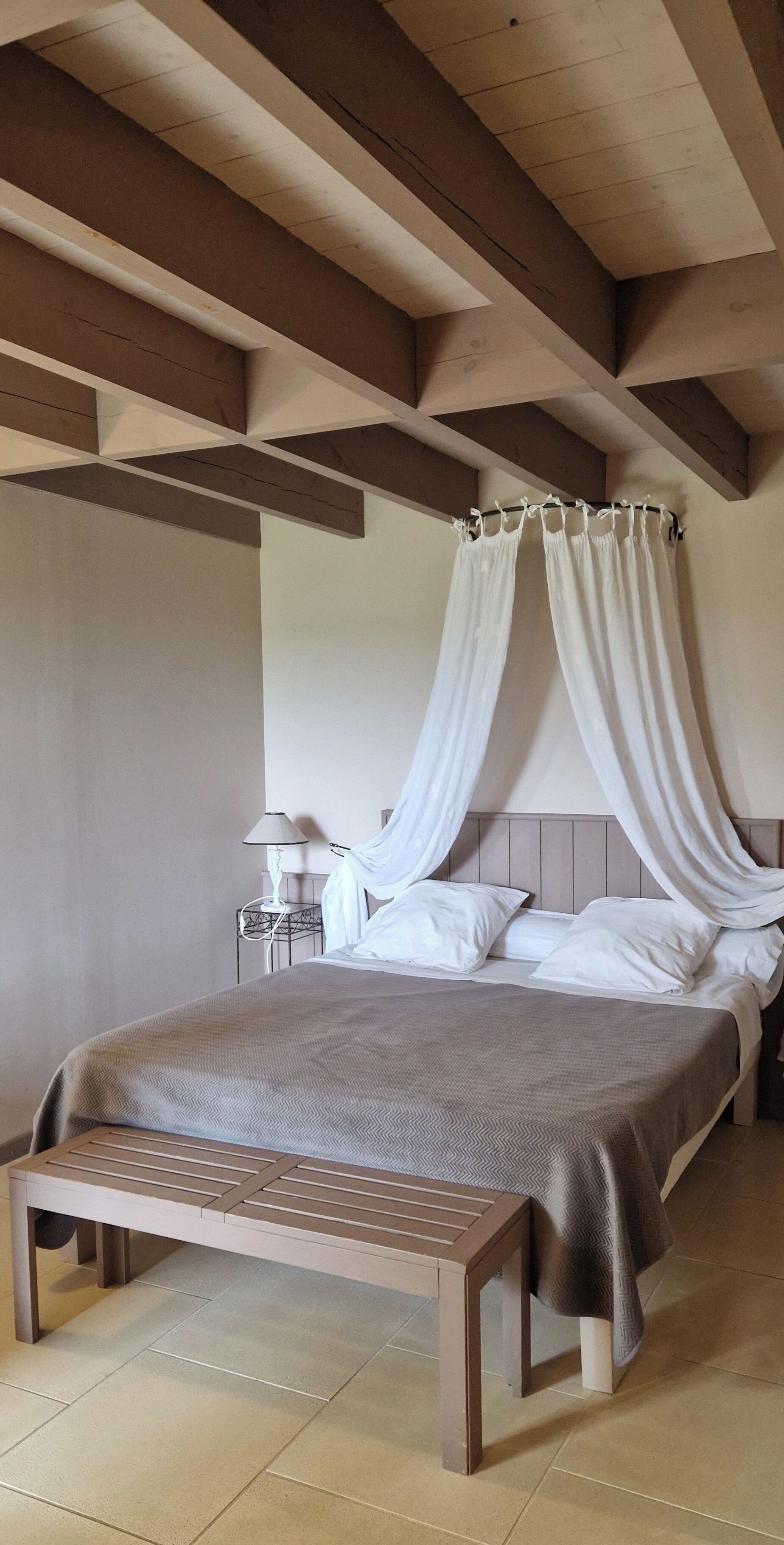 A bedroom with a bed, a bedside table, a lamp, and a bench.