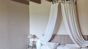 Een slaapkamer met een bed, nachtkastje, lamp en een bankje.