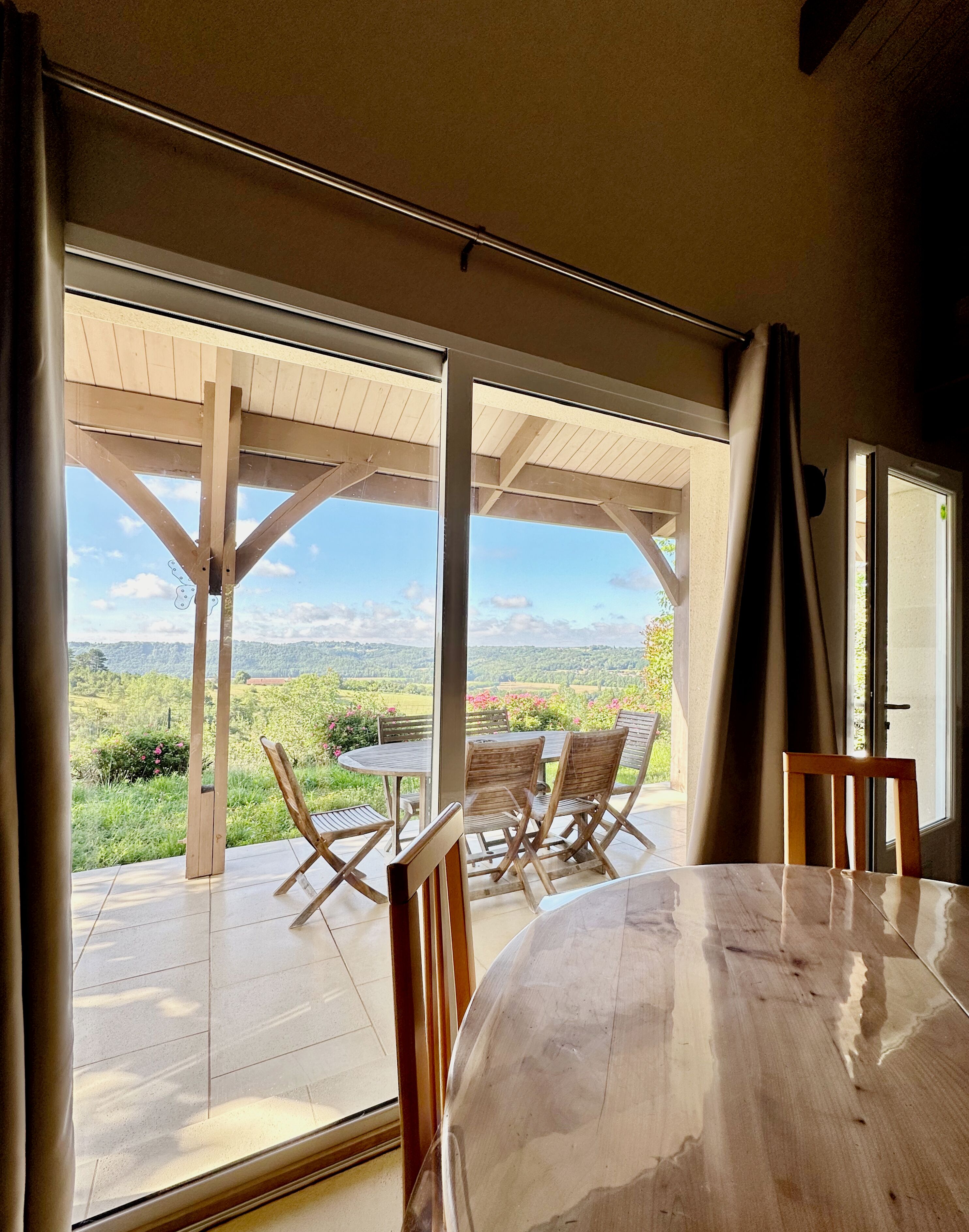 A dining area with a table and chairs, large windows, and a view of a green landscape.