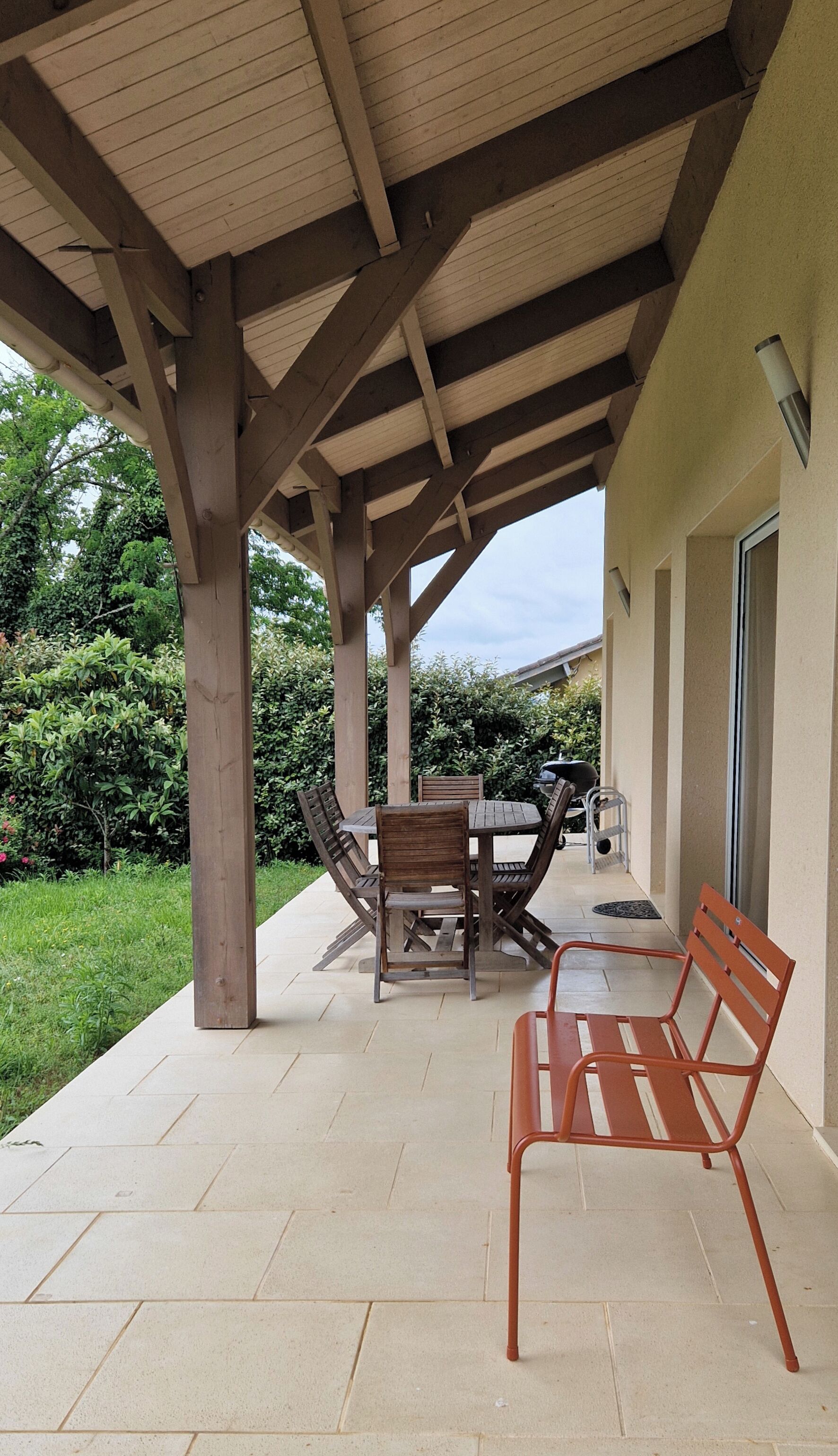 Une terrasse extérieure avec une table et des chaises en bois, un banc en métal et un barbecue.