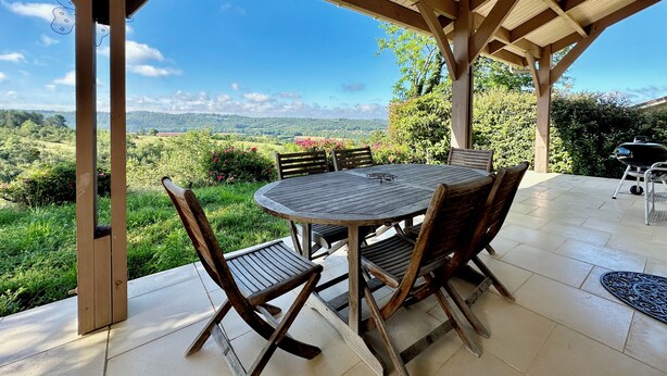 Een overdekt terras met een ronde tafel en stoelen, met uitzicht op een prachtig landschap.