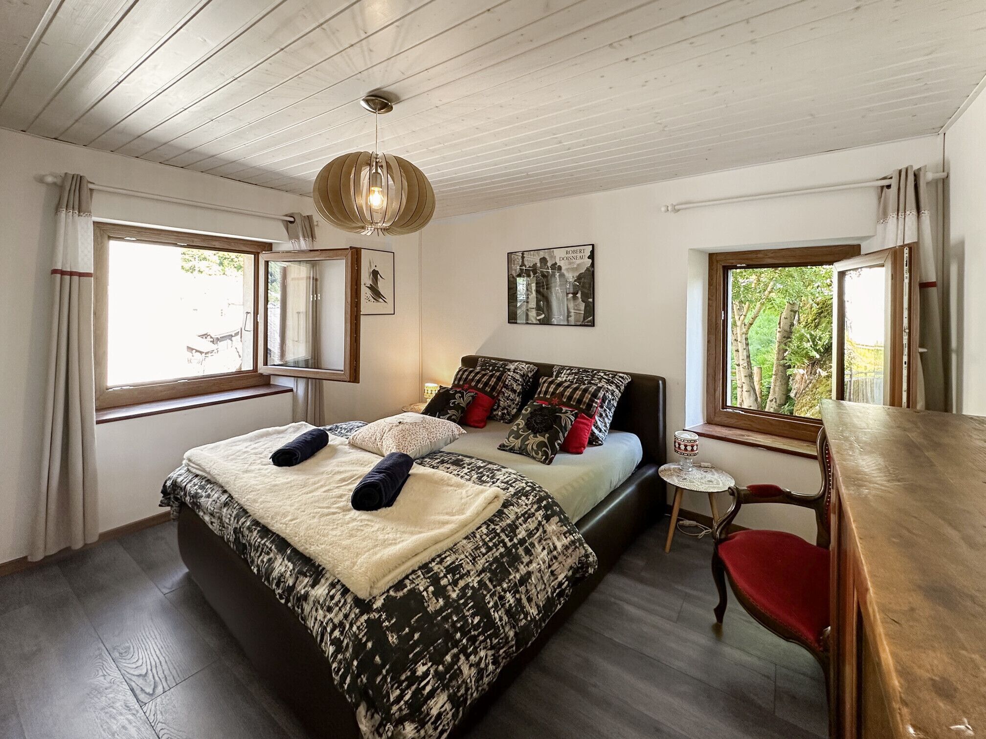 A bedroom with a bed, a bedside table, a chair, a window, and a ceiling light fixture.