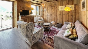 Una sala de estar acogedora con paredes y techo de madera, un televisor, un sofá, un sillón estampado y una alfombra roja con diseño.