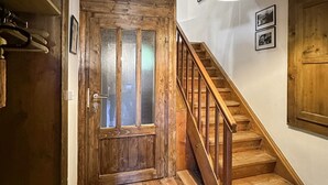Una escalera de madera que lleva a una habitación con puerta de madera y una lámpara colgante.