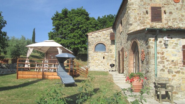 A stone building with a wooden deck, outdoor seating, and a covered area with a table and chairs. - Villa in Tuscany with Pool & Olive Groves (Castelnuovo di Val di Cecina (PI))
