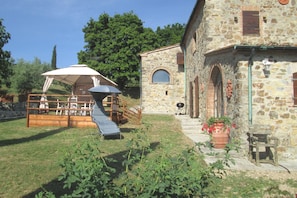 A stone building with a wooden deck, outdoor seating, and a covered area with a table and chairs. - Villa in Tuscany with Pool & Olive Groves (Castelnuovo di Val di Cecina (PI))
