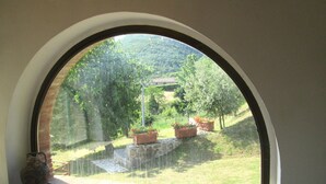 A view through a window with a stone ledge, a rustic vase, and a landscape with trees and a distant building. - Villa in Tuscany with Pool & Olive Groves (Castelnuovo di Val di Cecina (PI))