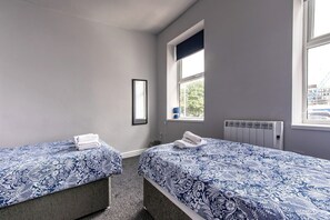 Una habitación con dos camas, un radiador, una ventana y un cuadro en la pared.
