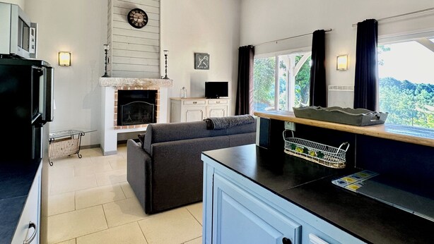 A modern kitchen with a built-in oven, a dining area with a sofa, and a large window offering a view of the outdoors.