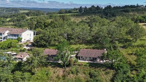 A rural landscape with three houses surrounded by dense greenery and hills in the background.