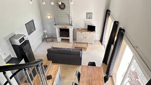 A spacious living area with a fireplace, dining table, and seating. A lofted space is visible above with a staircase.
