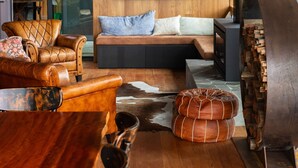 A modern living room with a wooden floor, leather sofa, and a large flat-screen TV mounted on the wall. - Loft Summary:<br>Within (Bangalow)