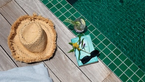 A wooden deck with a straw hat, a book, sunglasses, and a drink with a garnish.