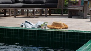 A poolside area with a lounge chair, a small table, and a hat on the edge of the pool. - Balaka Exclusive Property (Bangalow)