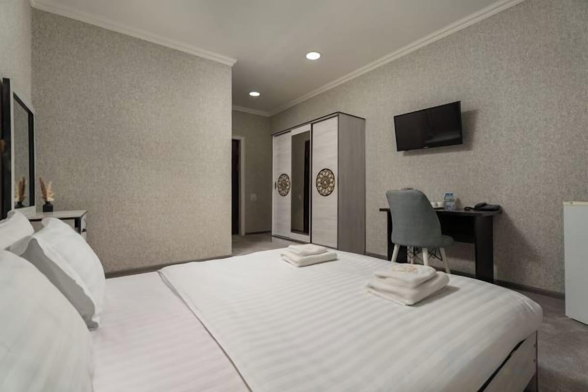 Una habitación de hotel con una cama grande, un escritorio, una silla, un televisor y un armario.