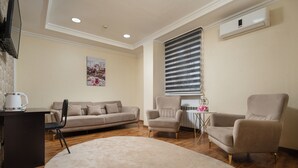 A living room with a sofa, two armchairs, a coffee table, and a TV mounted on the wall. - SV Stable Visitor Hotel (Tashkent)