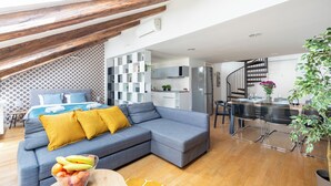 Een moderne woonkamer met een grijze hoekbank, een eethoek met een glazen tafel en een keuken op de achtergrond.