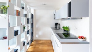Een moderne keuken met witte kasten, een zwart aanrecht en een ingebouwde kookplaat. Er staan potplanten op de planken en een fruitschaal op het aanrecht.