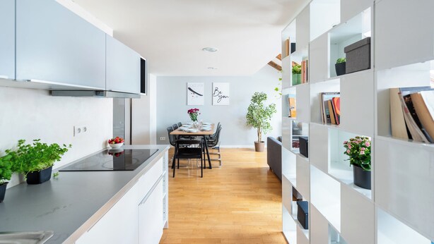 Een moderne keuken met witte kasten, een zwart aanrechtblad en een eethoek met een houten tafel en stoelen.