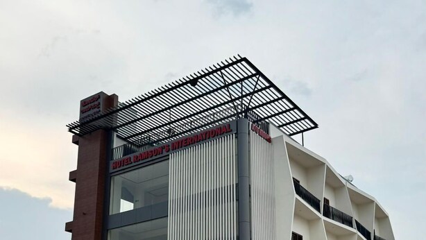 A multi-story building with a modern architectural design, featuring a prominent entrance with a metal canopy and signage for Hotel Ramsdon's International and Lodupri Sri Krishna Dayanand. - Hotel Ramsons International  (Hunsur)