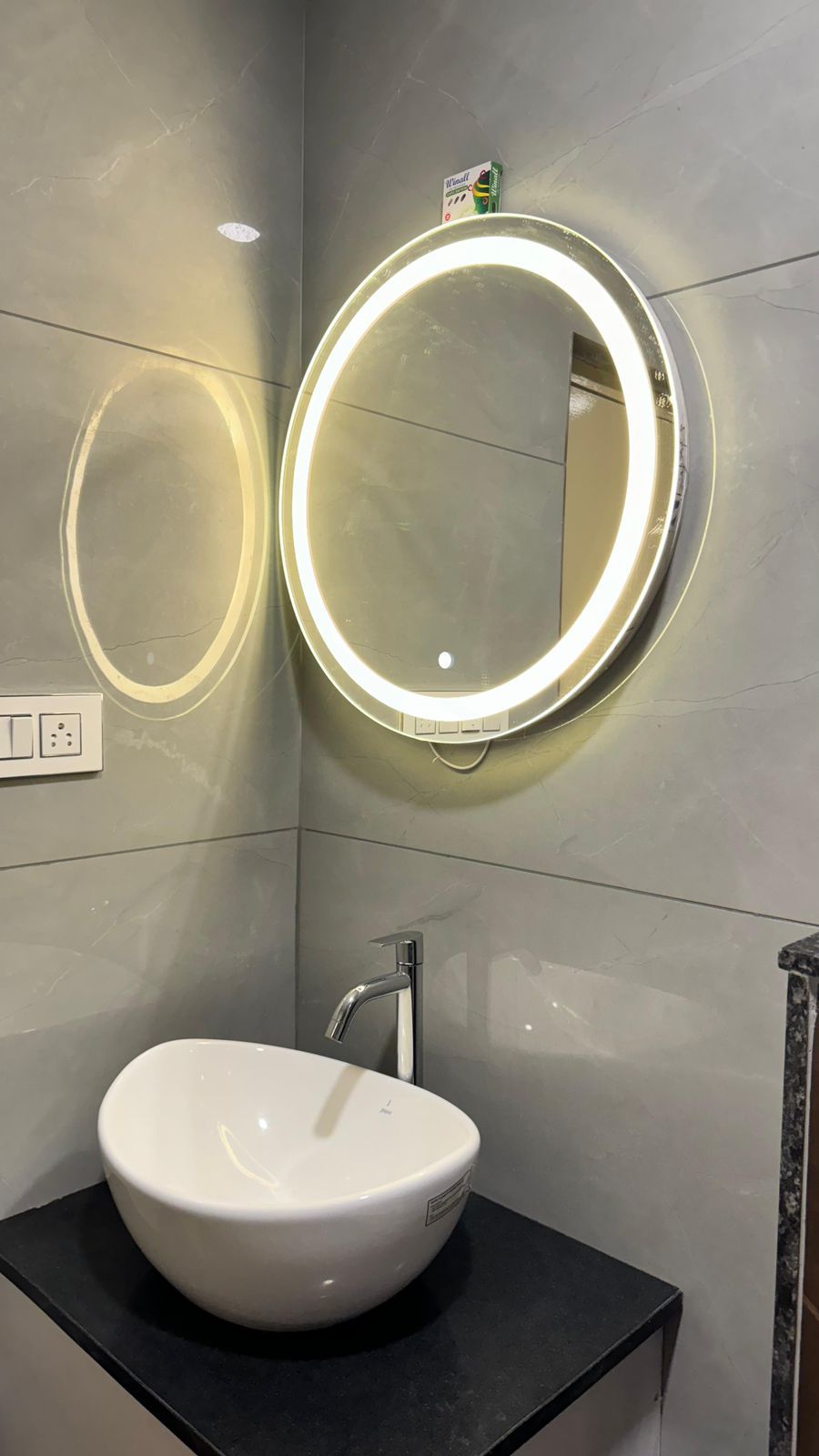Un baño con un lavabo blanco, un espejo redondo con luz y un perchero para toallas.