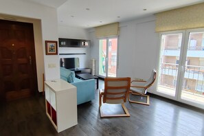 Un salon moderne comprenant un canapé, un fauteuil, une petite table et un coin cuisine avec des placards et un radiateur.